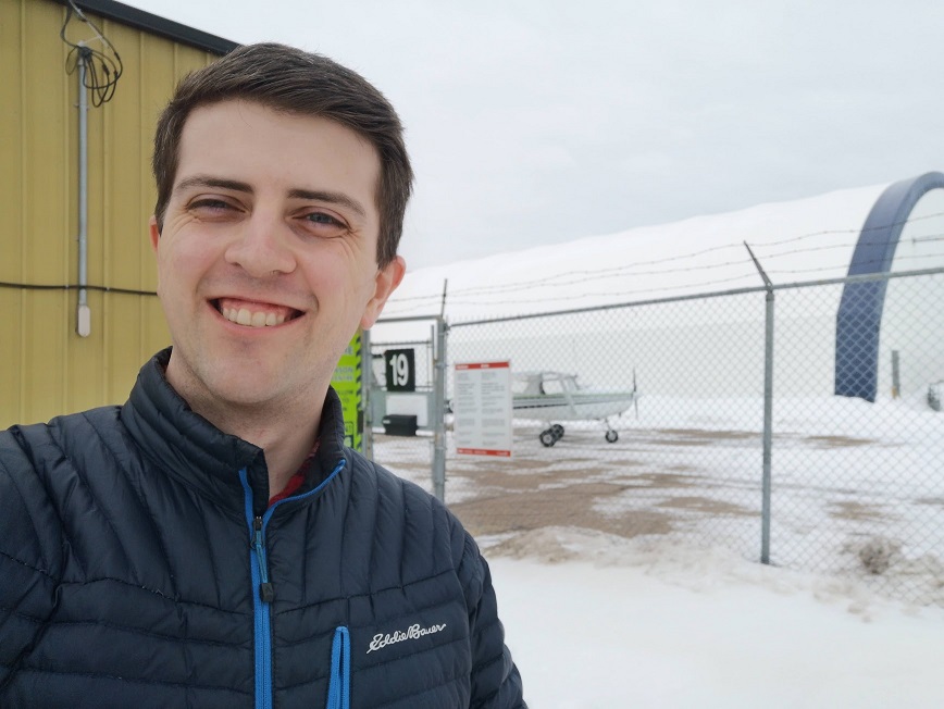 A selfie of a motion-sick person standing in front of a tiny plane